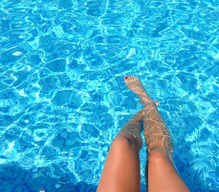 Woman's legs dangling in a swimming pool.