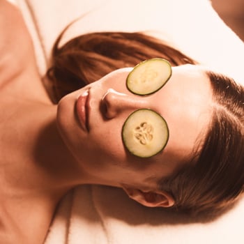 Face and shoulders of a woman relaxing during a facial with cucumbers covering her eyes
