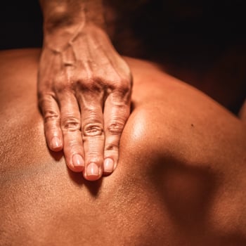 Massage therapist's hand working on the muscles underneath the shoulder blade of a massage guest at Viva Day Spa + Med Spa in Austin, TX.