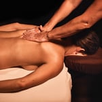 Woman lying face down receiving a back massage, with the licensed massage therapist's hands between the woman's shoulder blades.