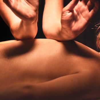 Close-up of a woman's back receiving a massage, with the massage therapist focusing beneath her shoulder blades.