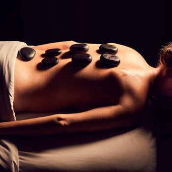 Profile image of a woman on a massage table with hot basalt stones on her back.