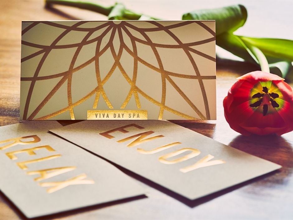 Classic gold foil Viva Day Spa gift certificate on a wood table, with envelopes options that read "Relax" and "Enjoy"