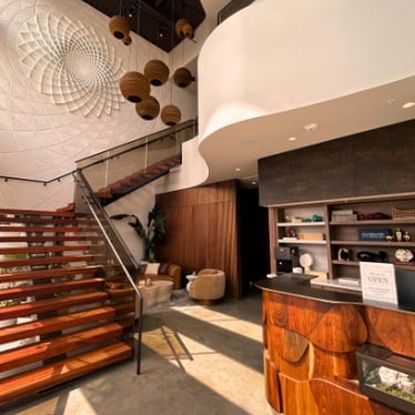 Spa lobby with sculptural mosaic art feature, hanging pendant lights, wood staircase, and reception desk at Viva Day Spa + Med Spa Dallas