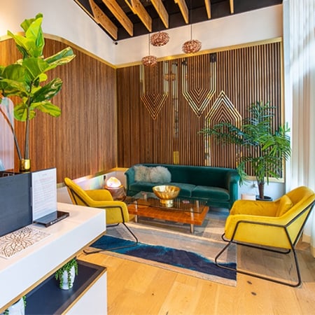 Upscale med spa lobby at Viva Day Spa + Med Spa at Domain Northside in Austin, TX, featuring a teal sofa, yellow accent chairs, warm wood-paneled walls, and modern pendant lighting