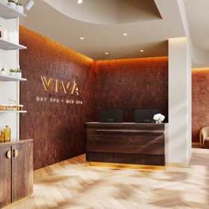 The reception area at Viva Day Spa + Med Spa Morningside in Atlanta, GA, feels warm and inviting with a wood desk, gold Viva signage, and softly illuminated walls.