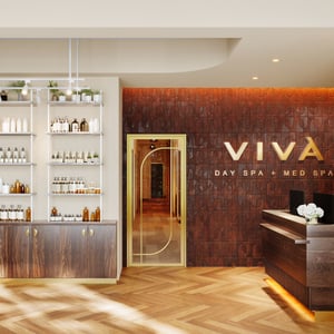 The lobby at Viva Day Spa + Med Spa Morningside in Atlanta, GA, welcomes guests with warm wood finishes, a gold-framed glass door, and professional skin care product displays.